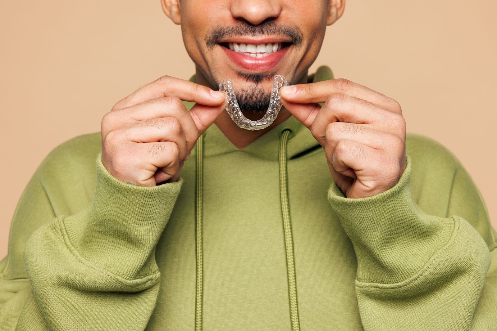 Smiling man holding clear aligner, showcasing its discreet design and suitability for orthodontic treatment.