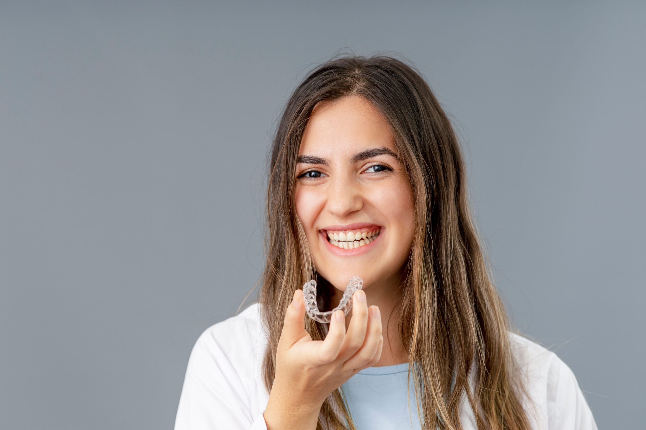 Smiling young woman holding clear dental aligner, showcasing adult orthodontic care options at Smile Island Dental Group in Rocklin.